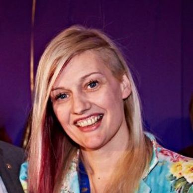 Female headshot, long blonde hair with pink undercolour.