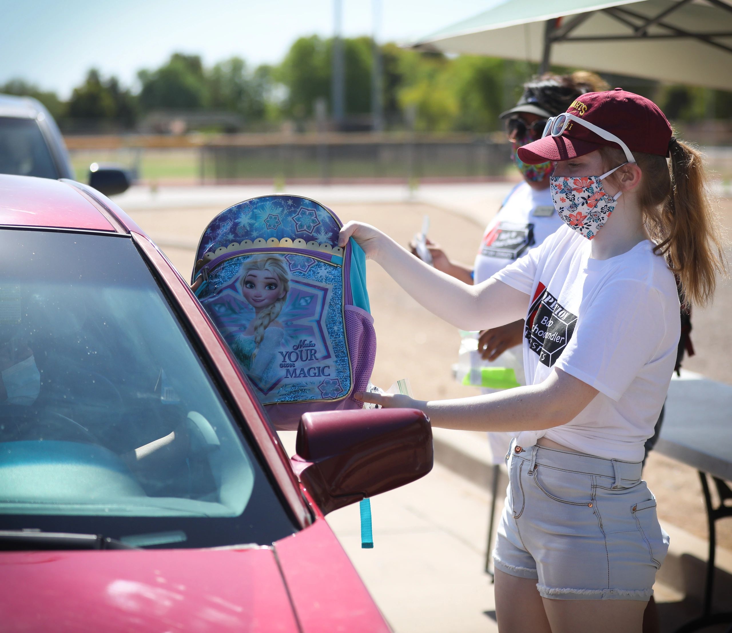 Girl giving a Frozen-themed backpack to a red car.