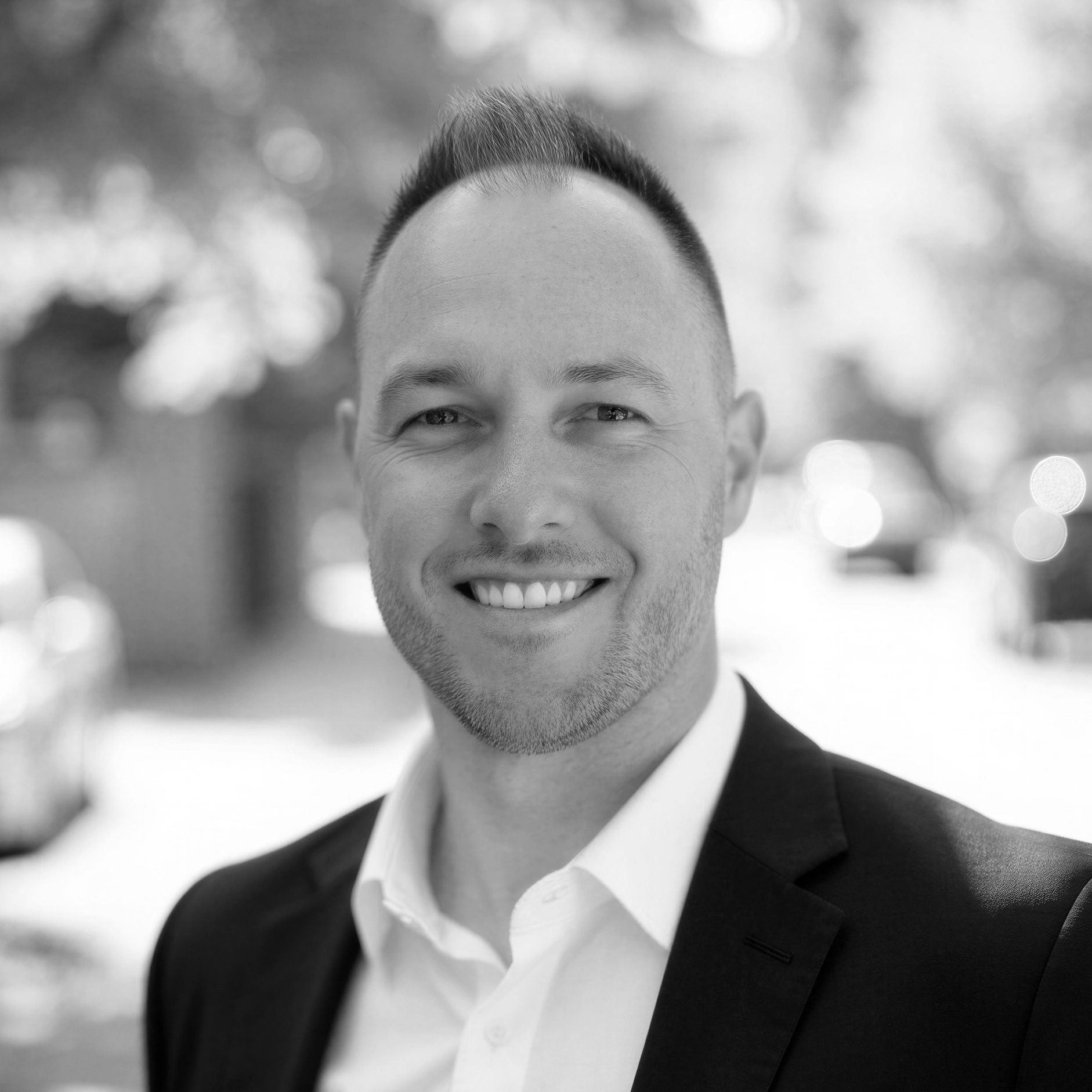 Close-up black and white portrait of a smiling man in a suit.
