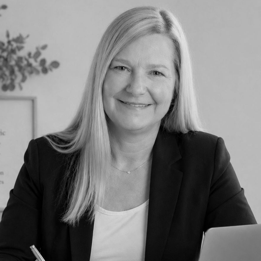 Smiling woman in business attire working at her desk with a laptop.