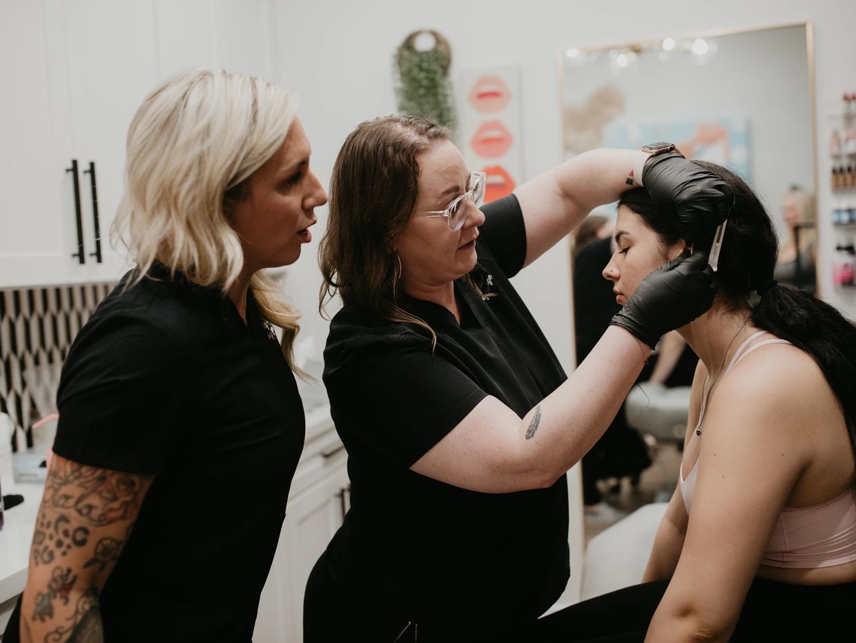 Two women training on ear piercing with a third woman as the model in a studio.