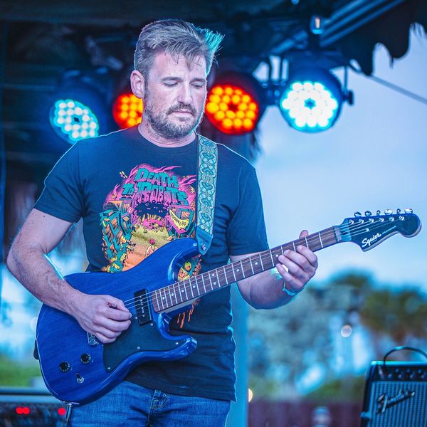 Man playing electric guitar on stage with colorful lights.