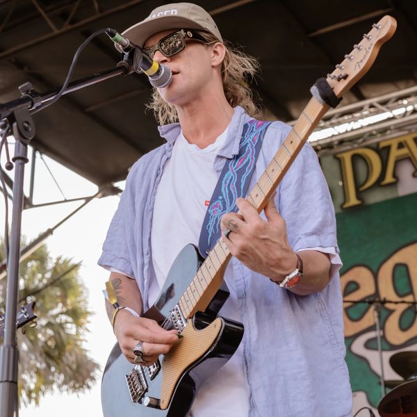 Musician playing guitar and singing on stage at an outdoor event.