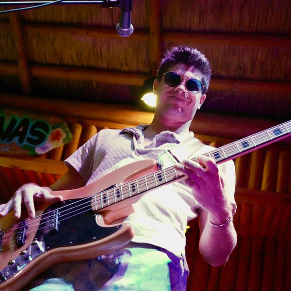 Man playing bass guitar on stage, smiling with sunglasses.