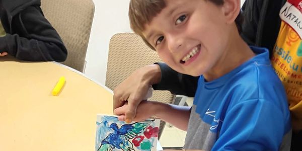 A boy smiling while holding a drawing of birds.
