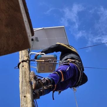 Worker climbing utility pole to install or maintain equipment under clear blue sky.