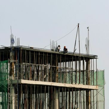 Two construction workers on top of an unfinished building structure.