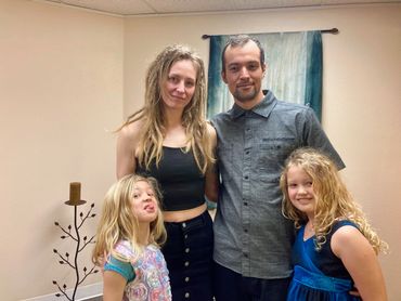 Whitney & Noah pose with their sweet young daughters, one with her tongue out, after their wedding