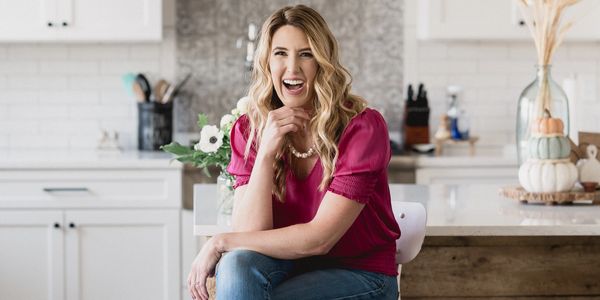 Woman in pink shirt  laughing sitting on stool in kitchen