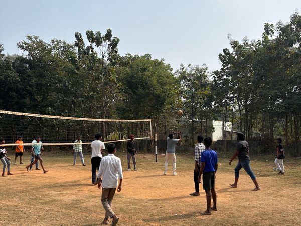 Group playing volleyball on a dirt court outdoors.