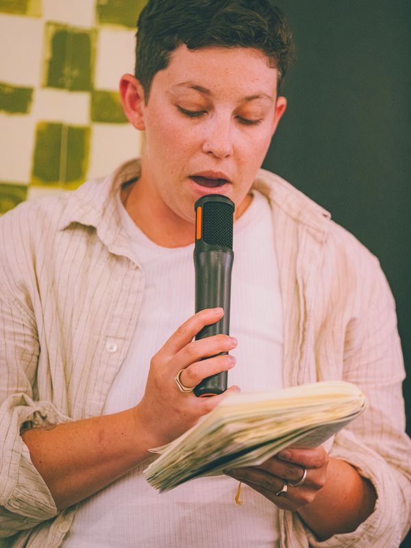 Person reading from a notebook into a microphone.
