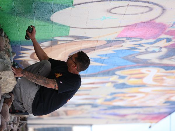 A man spray-painting a colorful mural on a wall.