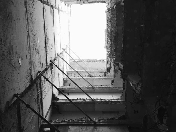 Black and white photo of an abandoned stairwell with exposed rebar and crumbling walls.