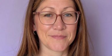 Woman with glasses smiling against a purple background.