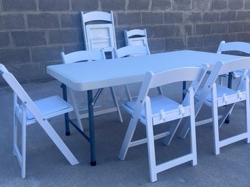 White folding chairs around a white folding table outside.