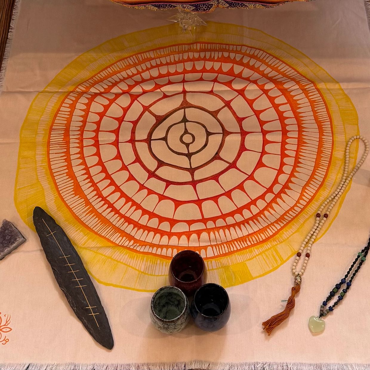 A colorful mandala cloth with cups, beads, and stones arranged on it.