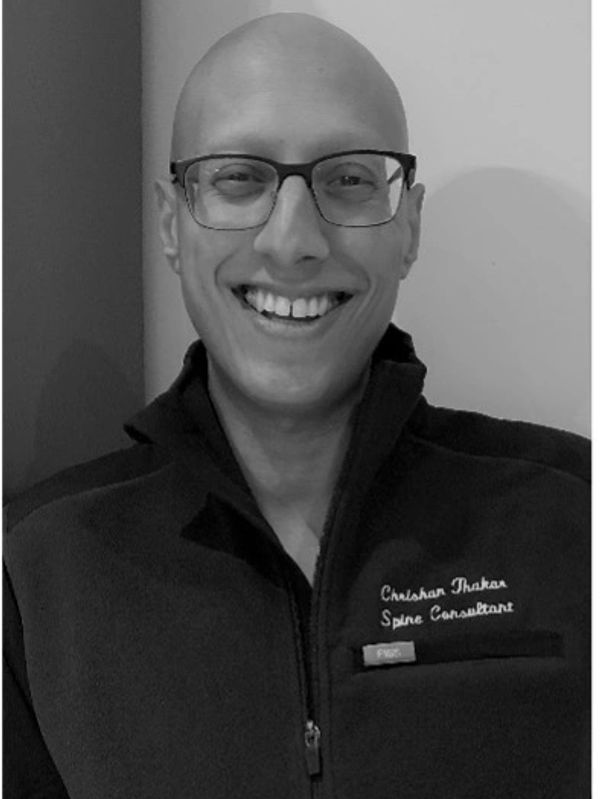 Smiling man with glasses wearing a jacket embroidered with 'Chirag Thaker Spine Consultant'.