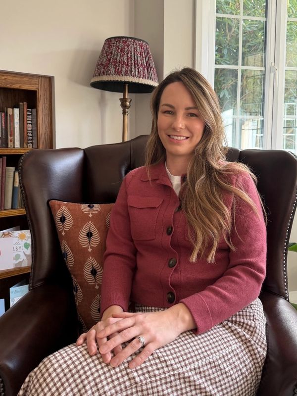 A woman in a maroon sweater sitting on a leather chair, smiling.