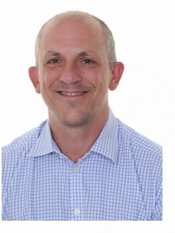 Smiling man in a blue checkered shirt against a white background.