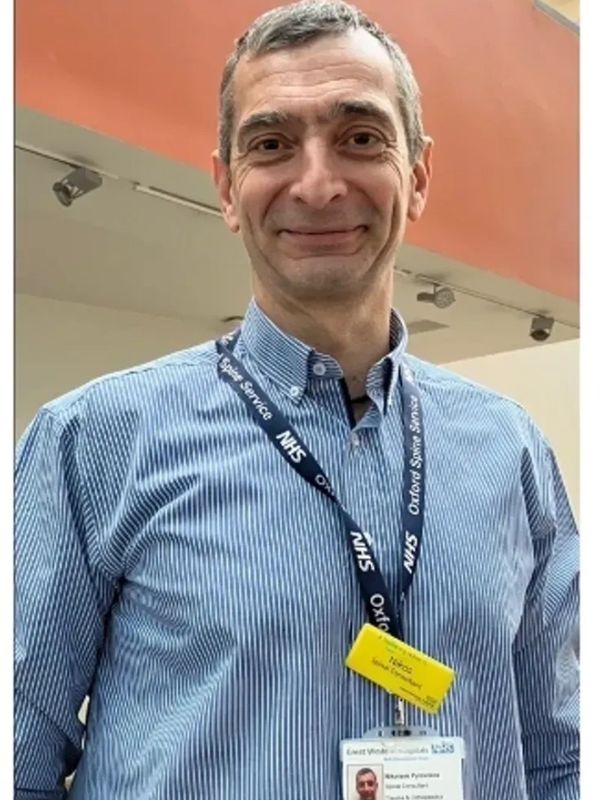Man wearing NHS badge and blue striped shirt smiling.