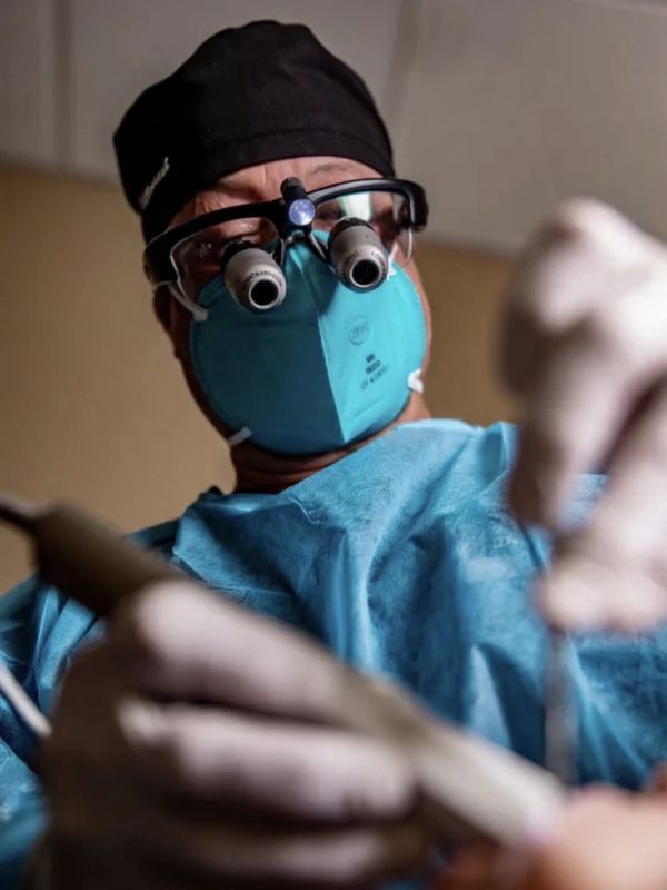 Dentist wearing magnifying glasses and mask performing a dental procedure.