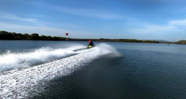 Person riding a jet ski on calm blue water under a clear sky.
