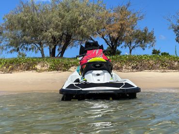 Jet ski beached on a sandy shore with trees and clear blue sky.