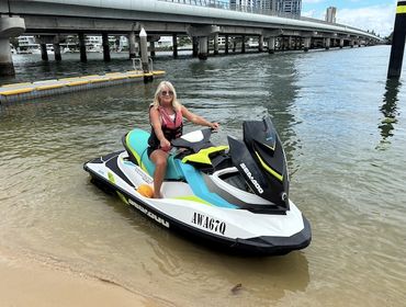 Woman sitting on a Sea-Doo jet ski near a bridge on a sunny day.