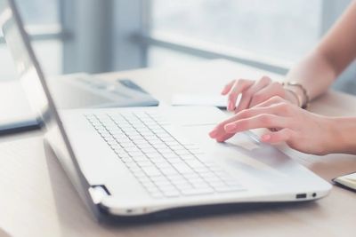 Hands typing on a laptop keyboard at a desk.