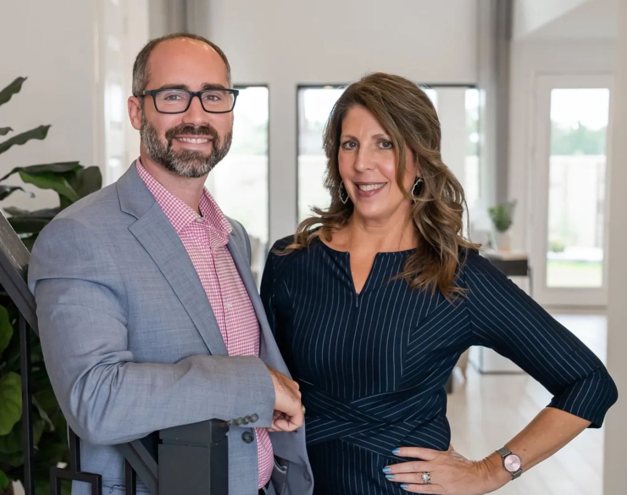 A professionally dressed man and woman smiling indoors.