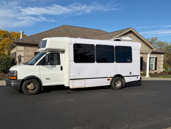 White shuttle bus parked in a residential driveway on a sunny day.