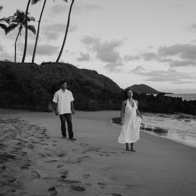 Couple walking on a beach at sunset in black and white.