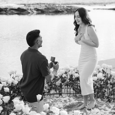 Man proposing to woman in a rose garden by the water.