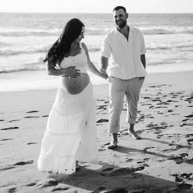 Pregnant couple walking hand-in-hand on the beach.