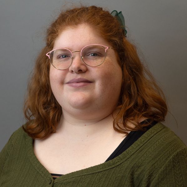 Portrait of a smiling woman with red hair and glasses wearing a green sweater.