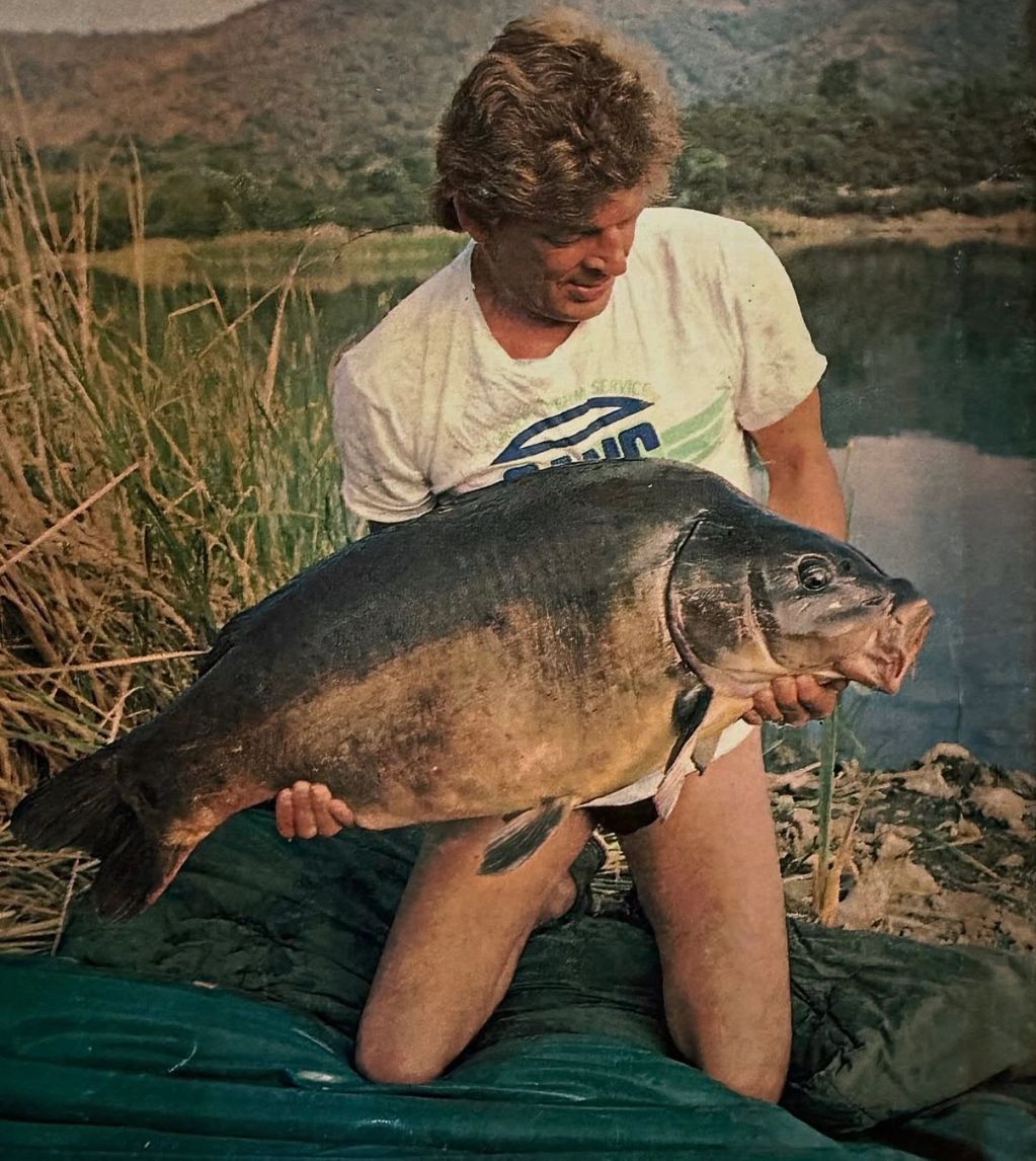 Man holding a large fish by a lake.