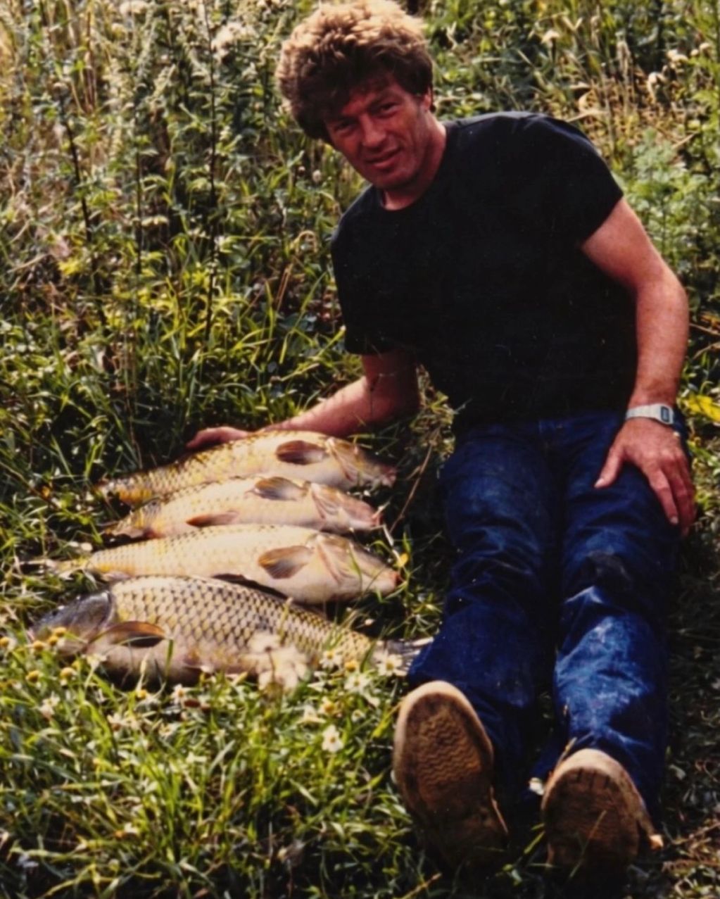 Man lying on grass with four large fish.