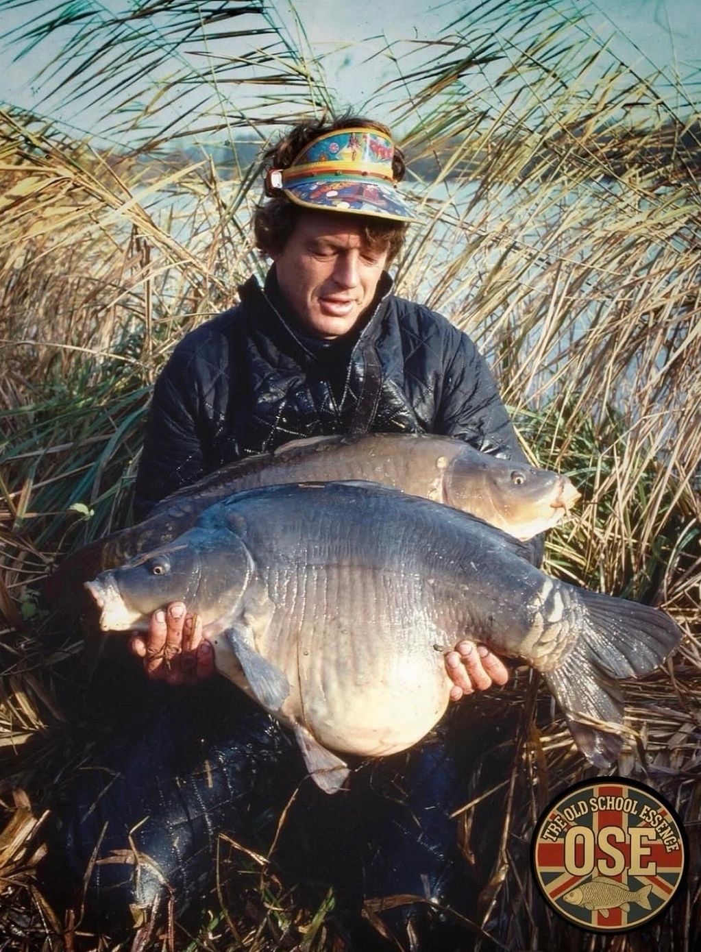 Fisherman holding two large fish near a lakeside.