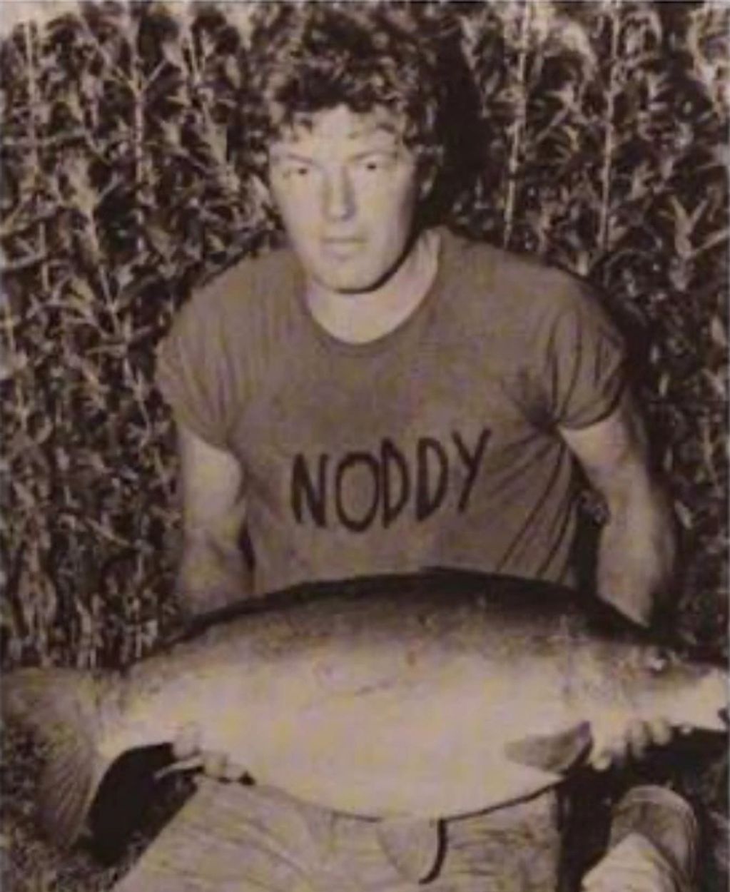 Man holding a large fish wearing a 'NODDY' shirt.