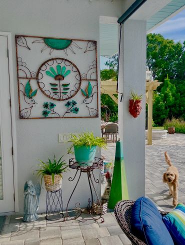 Cozy patio corner with decorative plants, wall art, and a dog walking by.
