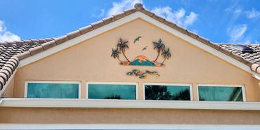 Decorative tropical-themed wall art above triangular windows on a house.