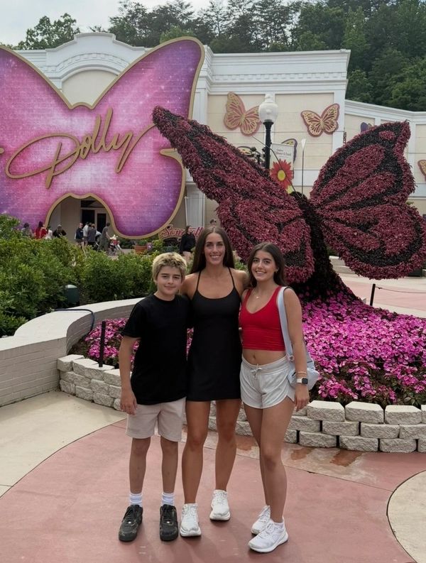 Three people posing in front of a giant butterfly floral sculpture at Dolly Parton's theme park.