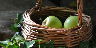 Two green apples in a woven basket surrounded by green leaves.