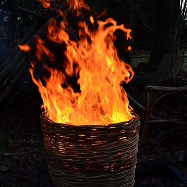 Bright orange flames burning in a woven basket outdoors at night.