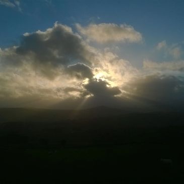 Sunset with sun rays piercing through dark clouds over a mountainous horizon.