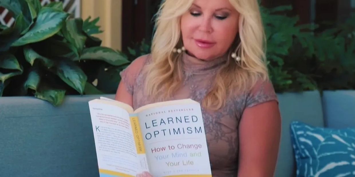 A woman reading the book "Learned Optimism" on a couch outdoors.