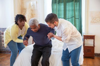 Care staff assisting man from bed