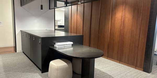 Modern office space with black desk, beige stools, and wooden panel walls.
