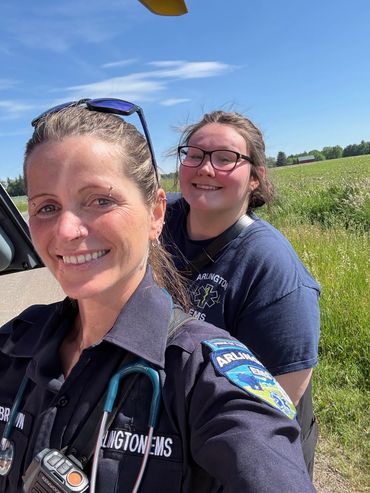Two smiling EMS personnel outdoors on a sunny day.