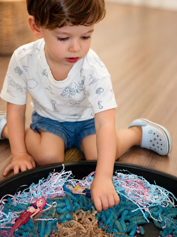 Young child playing with toy mermaids in sensory bin.
